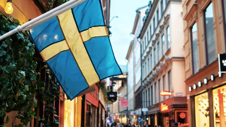 En svensk flagga hänger utanför en affär på en gata med butiker. Foto.