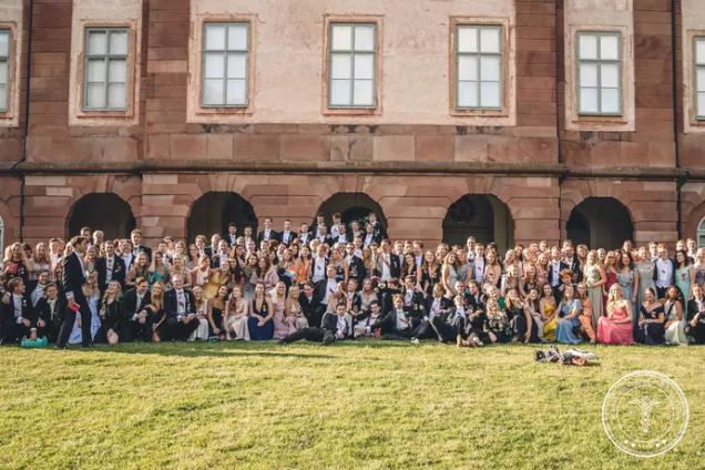 En stor grupp balklädda studenter i solen. Foto. 