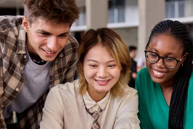 Glada studenter tittar tillsammans på en laptopskärm. Foto