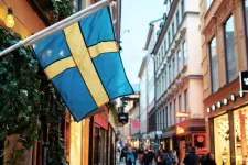 En svensk flagga hänger utanför en affär på en gata med butiker. Foto.