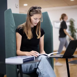 Student sitter i en fåtölj och läser. Foto. 